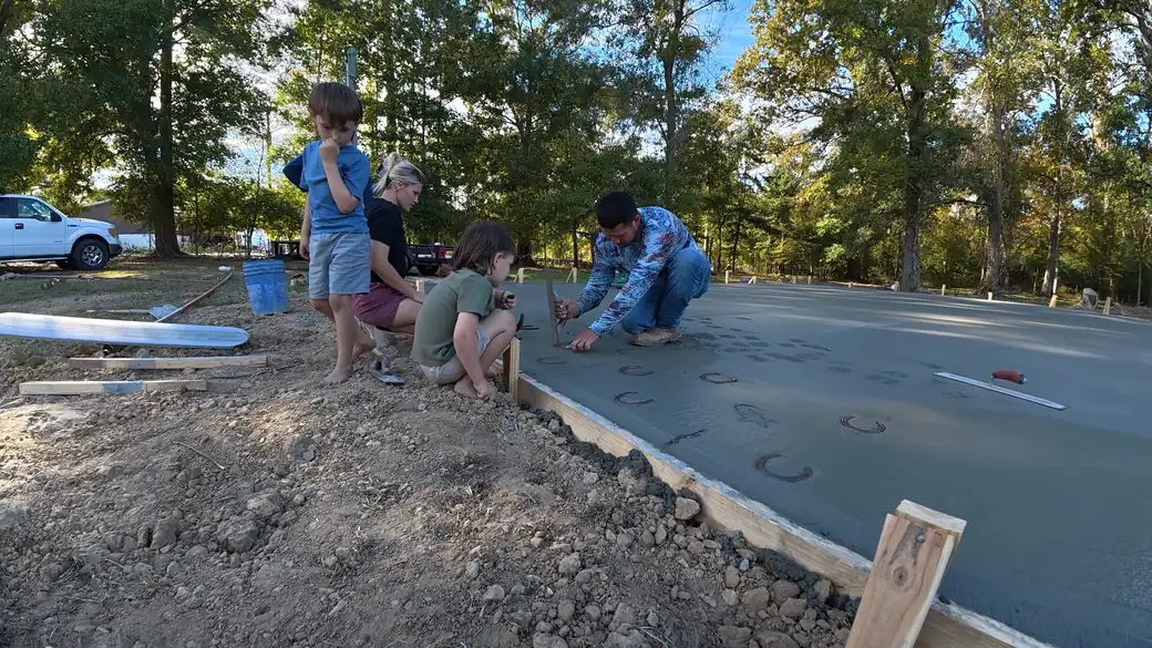 Family pressing horseshoes and handprints into their freshly poured concrete pad with a Parish Concrete Contractors finisher